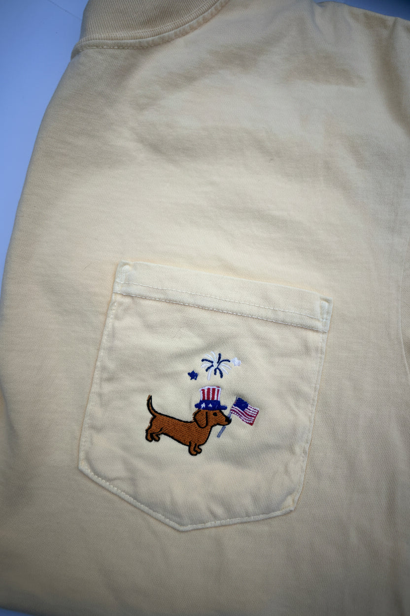 Beige shirt with a pocket featuring an embroidered dachshund and flag design on a yellow shirt