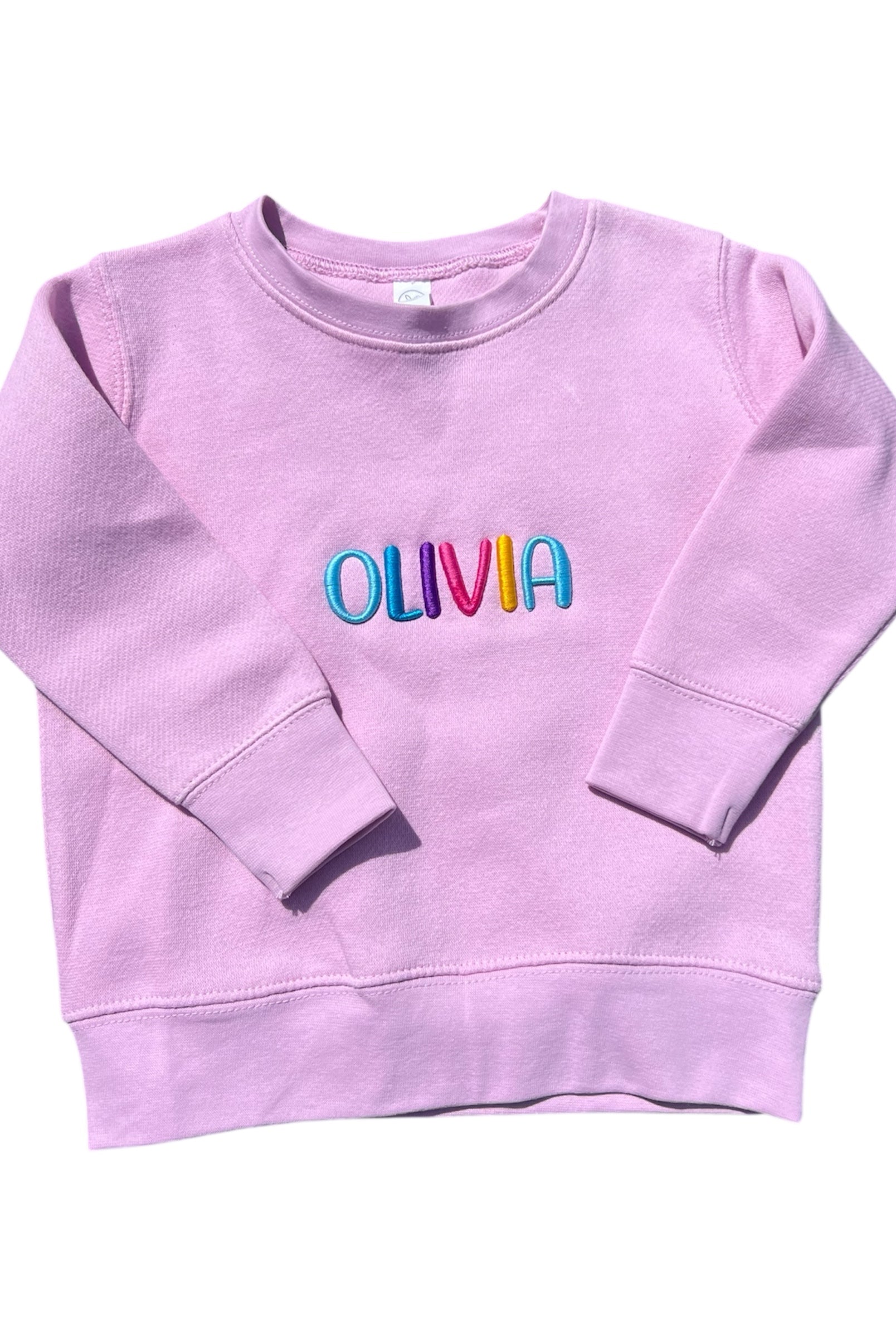 pink sweatshirt with 'OLIVIA' in colorful letters on a white background