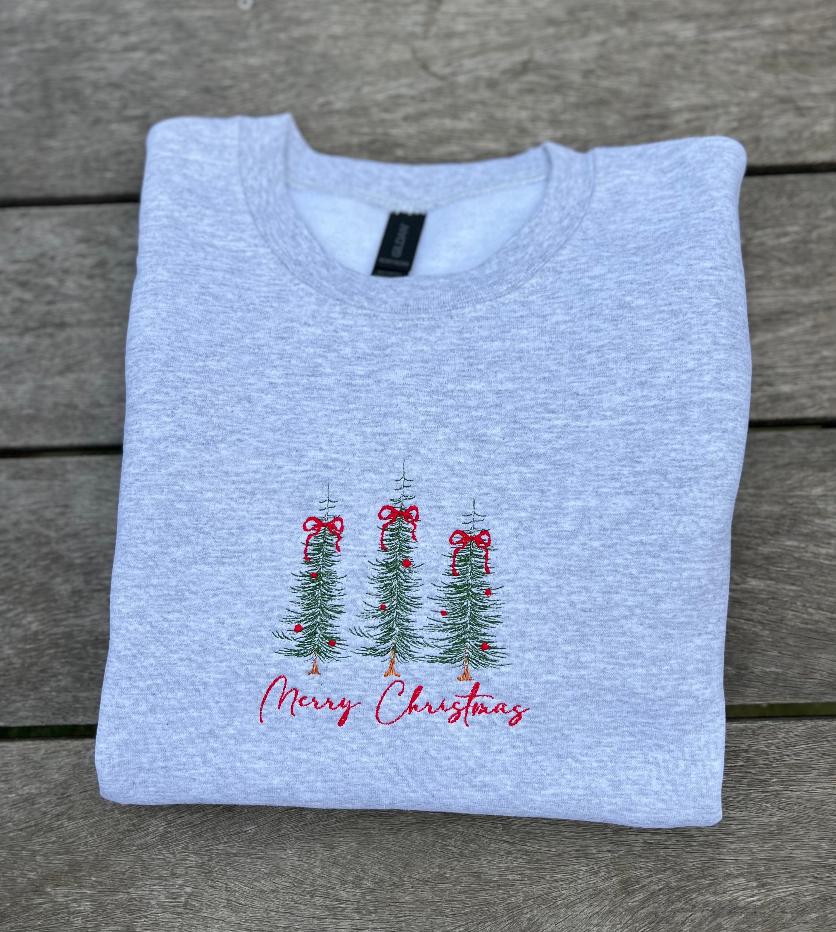 Folded light gray sweatshirt with Christmas tree and bow that says merry christmas on a wooden surface