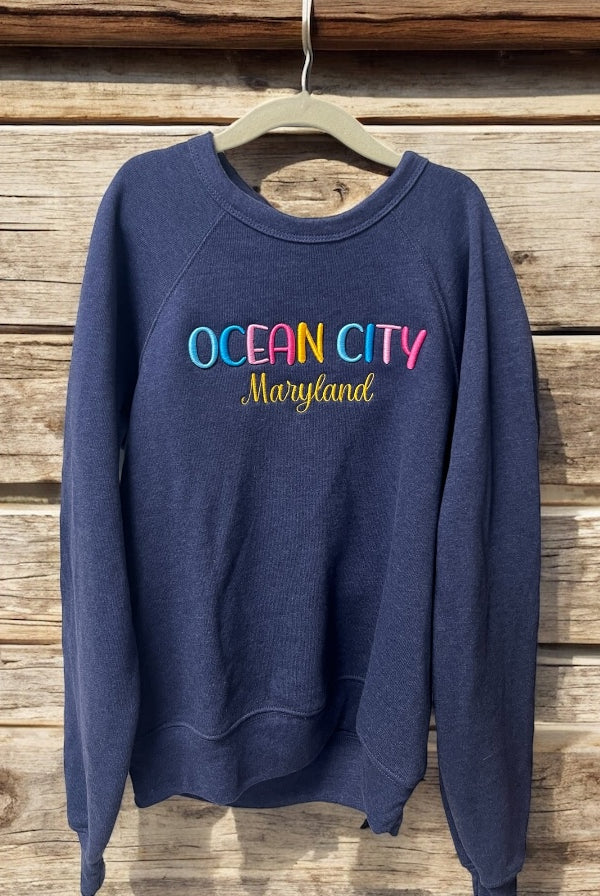 Navy blue sweatshirt with 'Ocean City Maryland' text on a wooden background