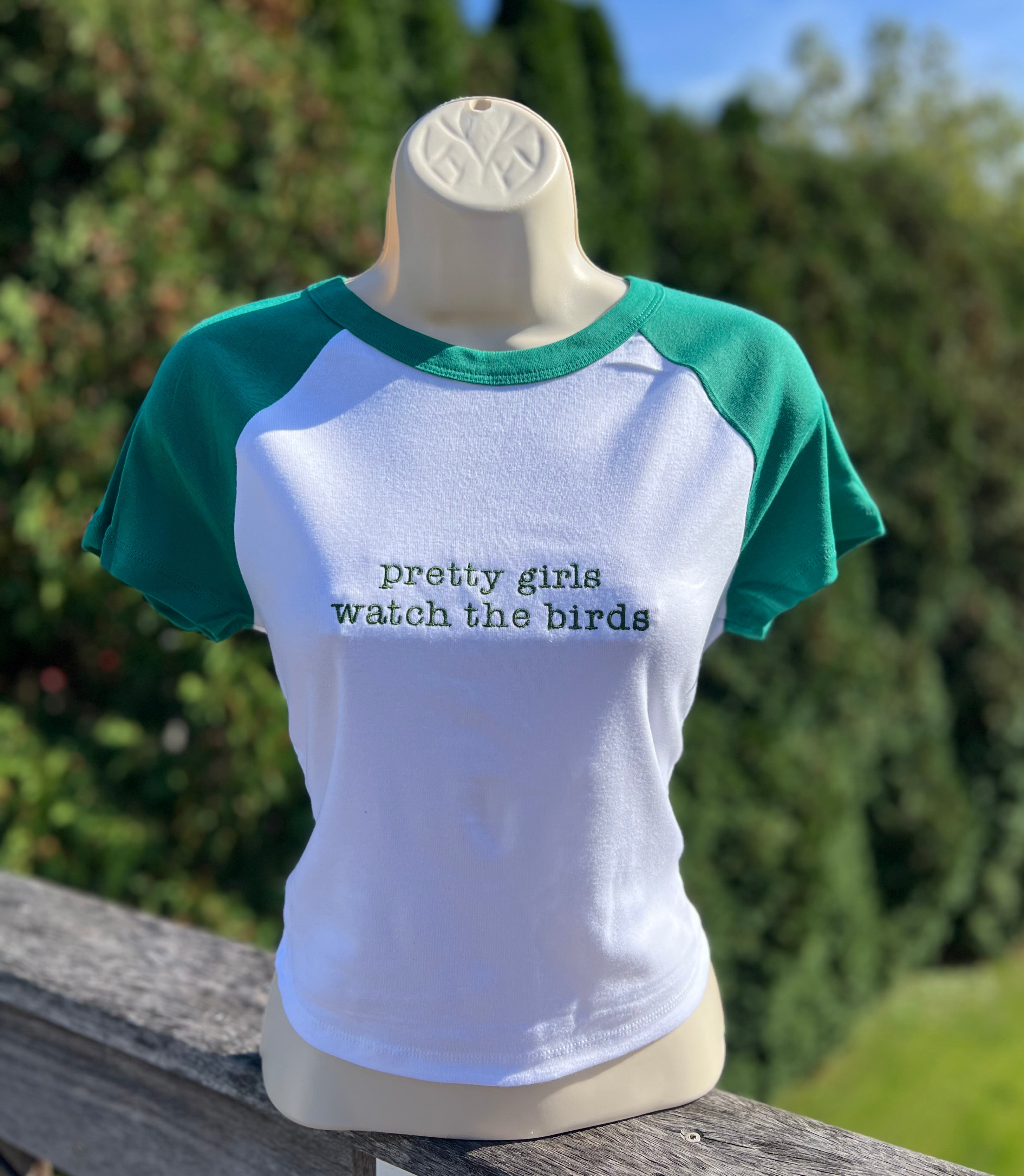 White cropeed t-shirt with green sleeves with pretty girls watch the birds embroidered on it