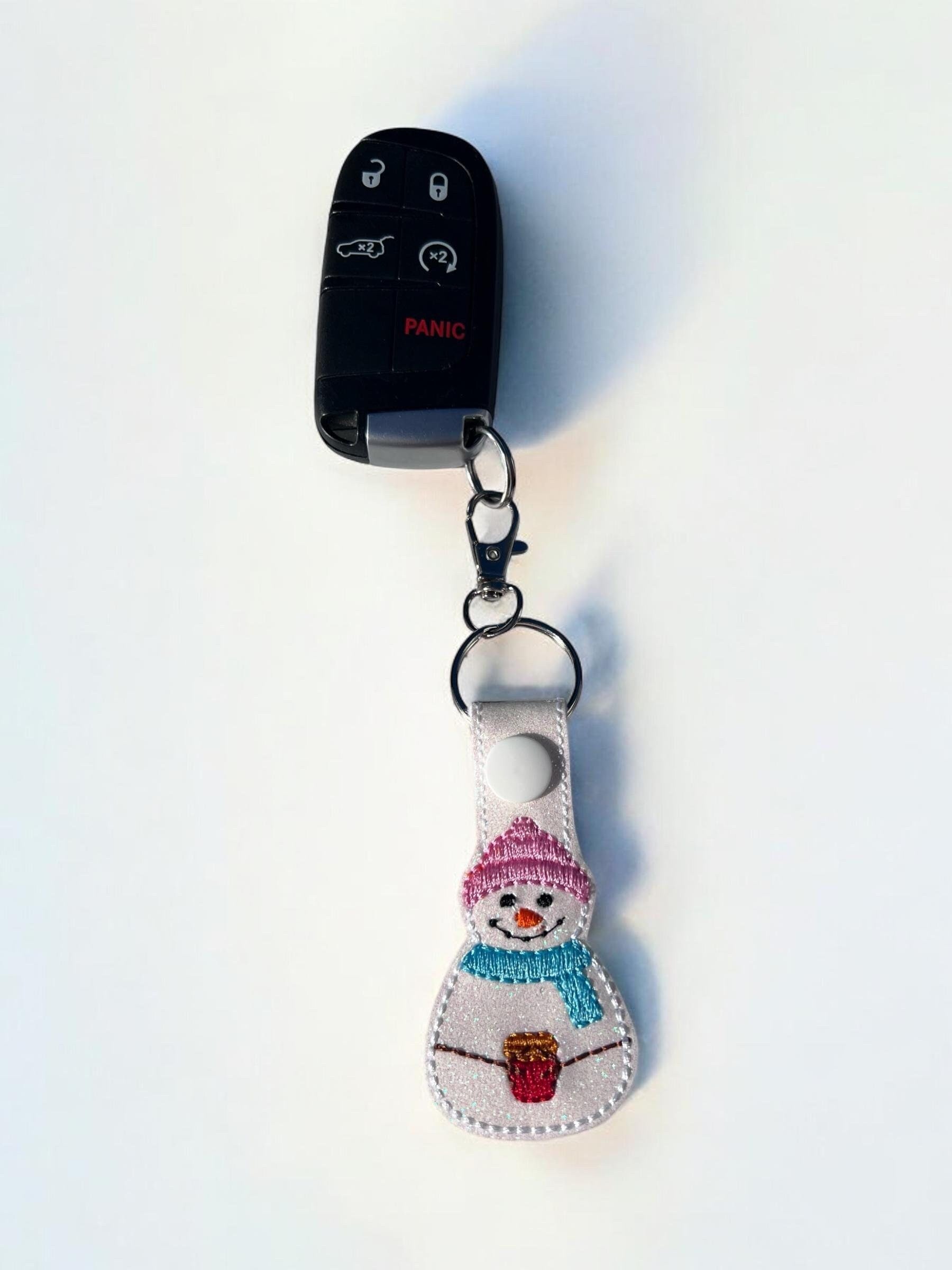 Keychain with snowman design attached to a car key fob on a white background