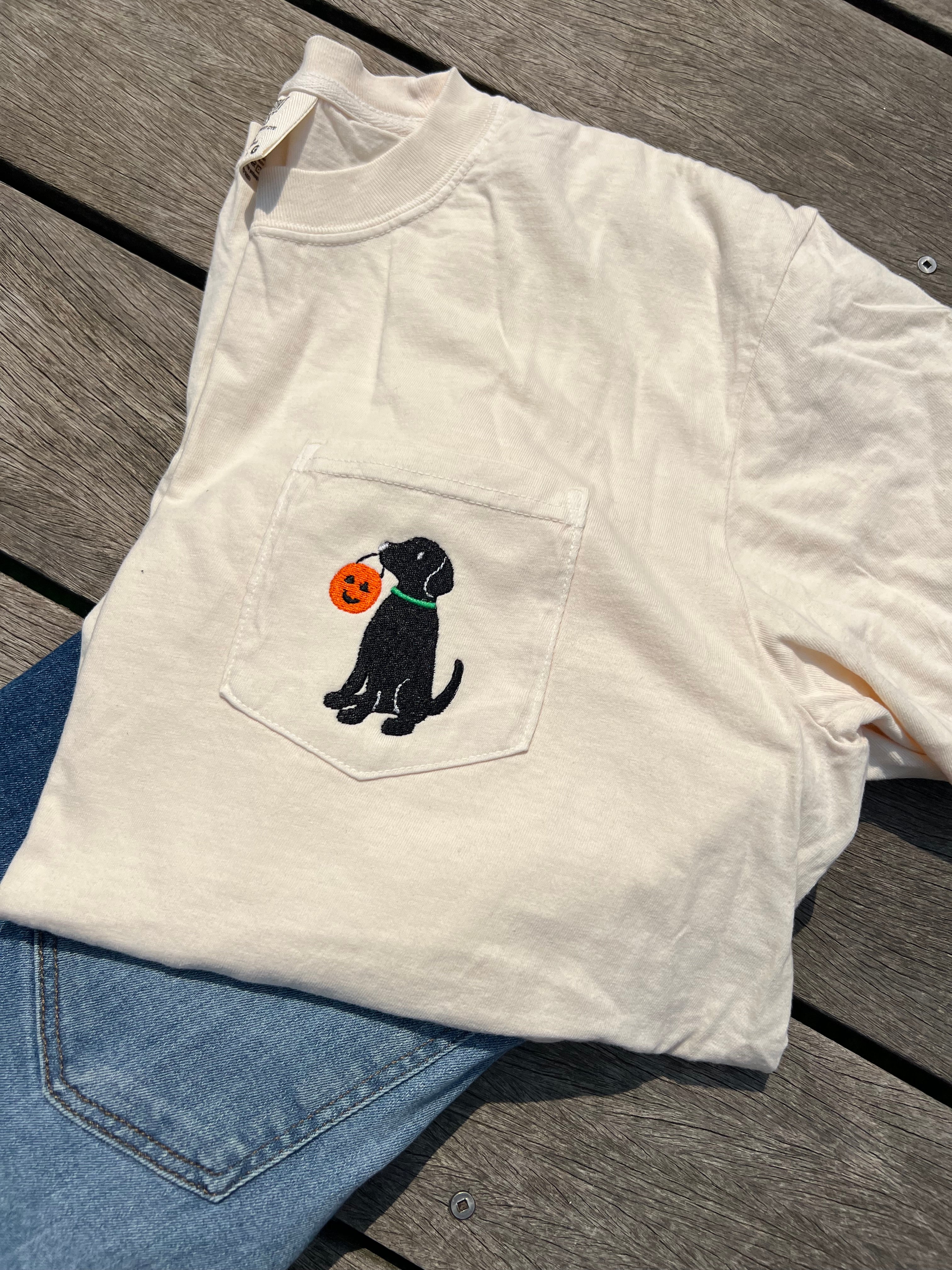 An off-white pocket t-shirt embroidered with a black dog holding an orange pumpkin