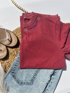 Red sweatshirt with 'America' text and star design on a white surface with denim jeans and sandals.