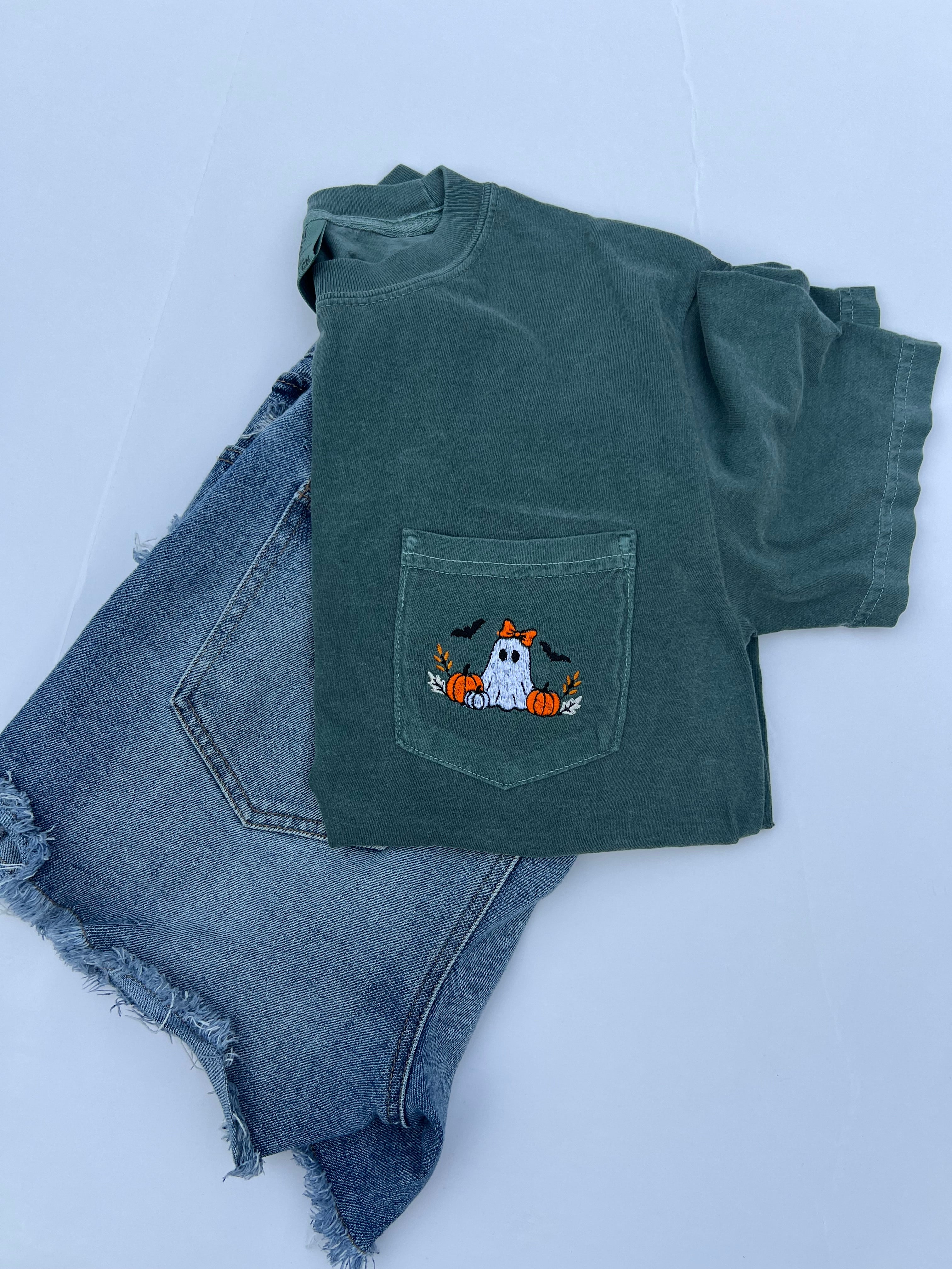 A dark green short-sleeve t-shirt with a front pocket featuring a cute embroidered ghost and pumpkin designbackground.