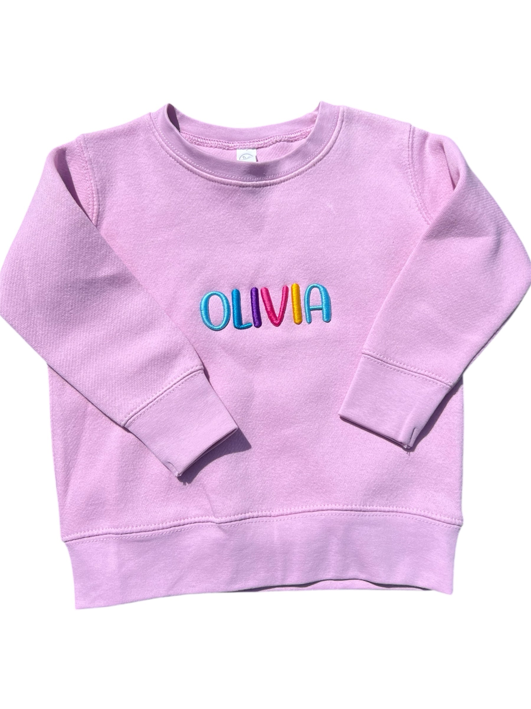 pink sweatshirt with 'OLIVIA' in colorful letters on a white background