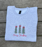 Folded light gray sweatshirt with Christmas tree and bow that says merry christmas on a wooden surface