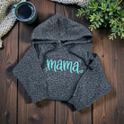 Gray leopard print hoodie with 'mama' text on a wooden surface with a cup and plant.