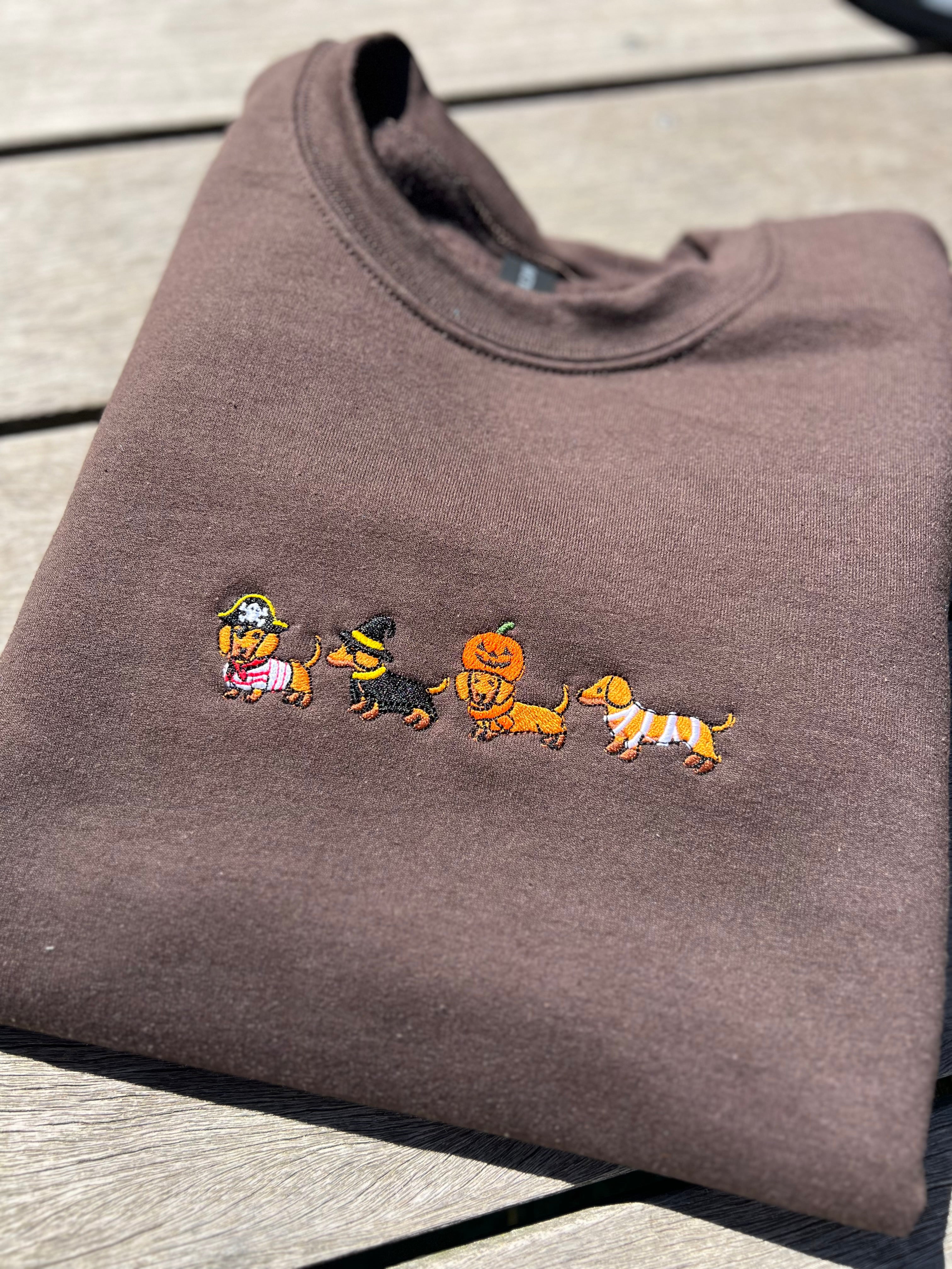 a brown sweatshirt embroidered with dachshunds wearing halloween costumes