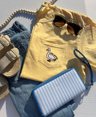 Yellow shirt with a duck design, sunglasses, blue jeans, and a striped wallet on a light gray surface.