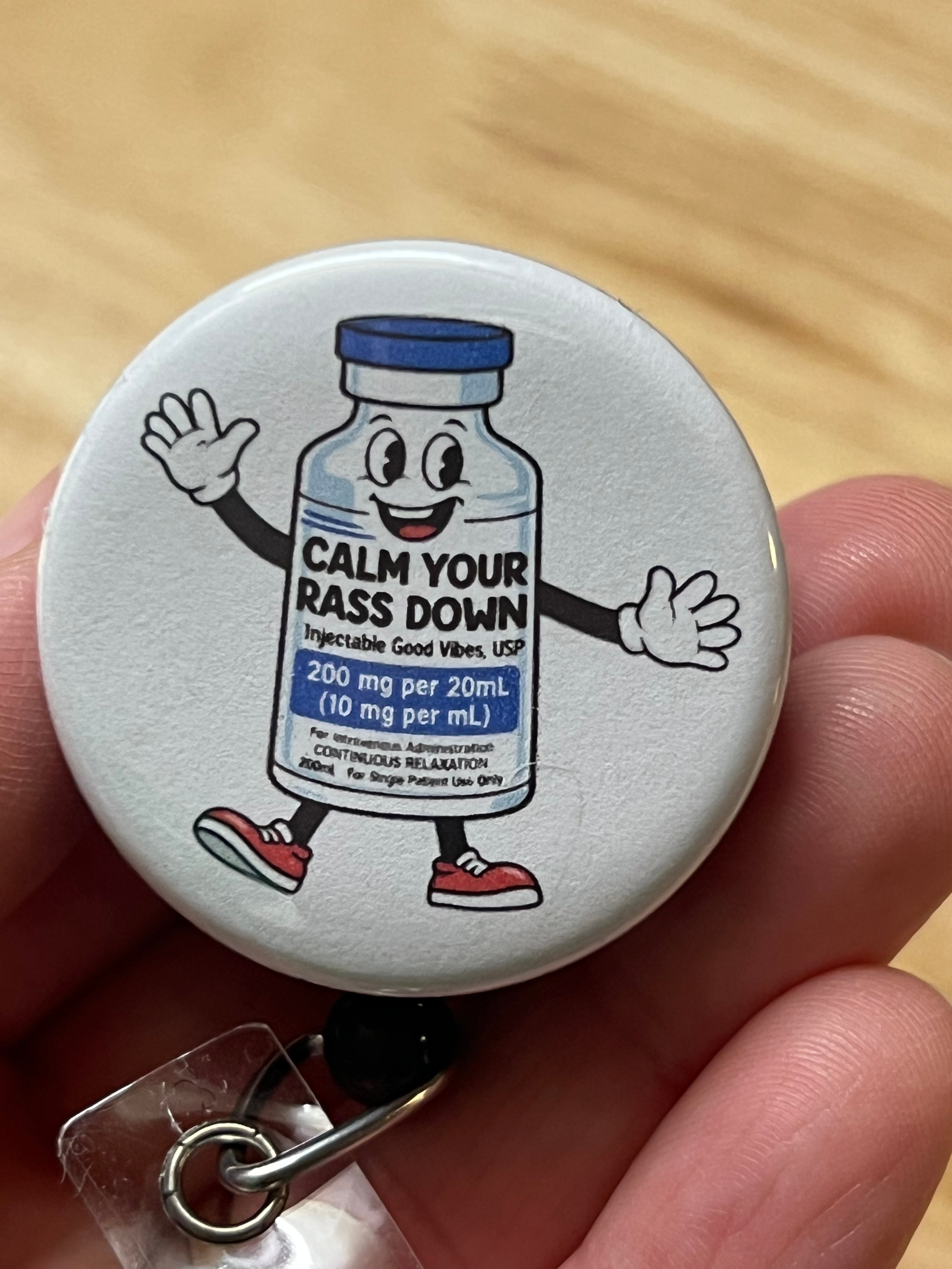 Button badge with cartoon character and text 'Calm Your Rass Down' held by a hand.
