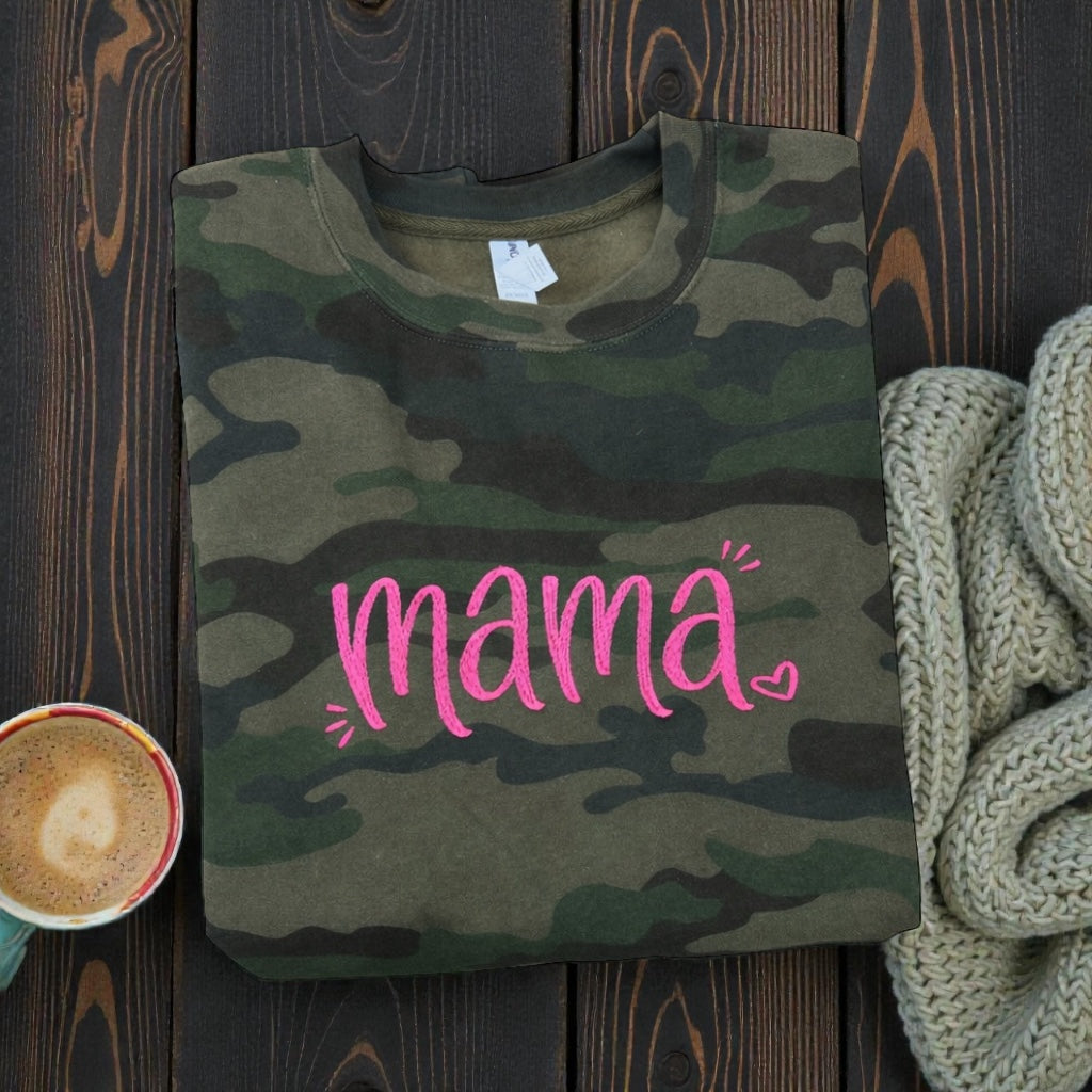 Camouflage t-shirt with 'mama' in pink on a wooden surface with a cup and blanket.