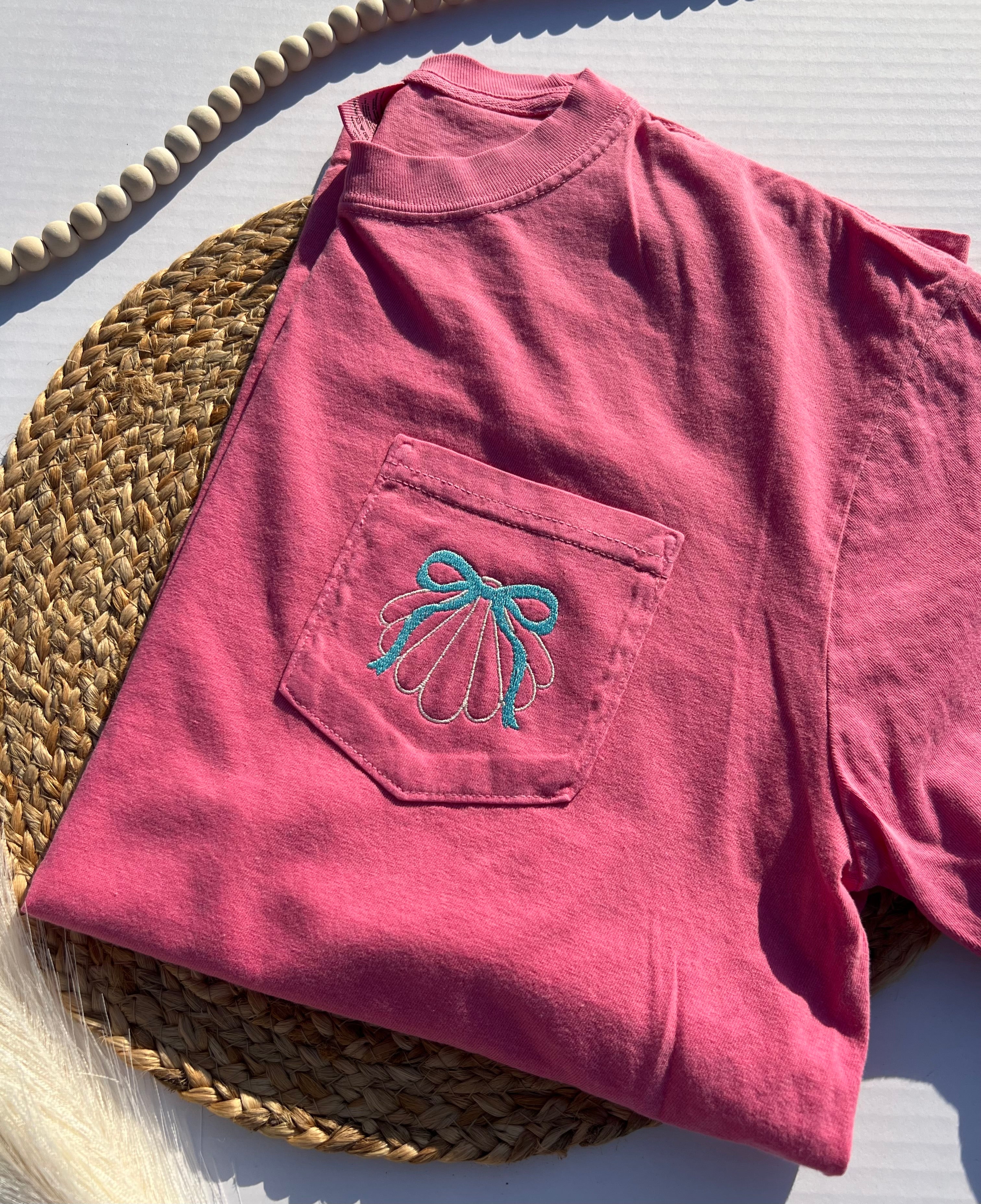 Pink t-shirt with a blue bow design on a woven mat