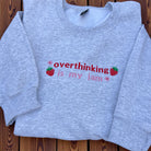 Gray sweatshirt with 'overthinking is my jam' text on a wooden surface