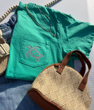 Green t-shirt with turtle design, straw bag, and sandals on a light surface