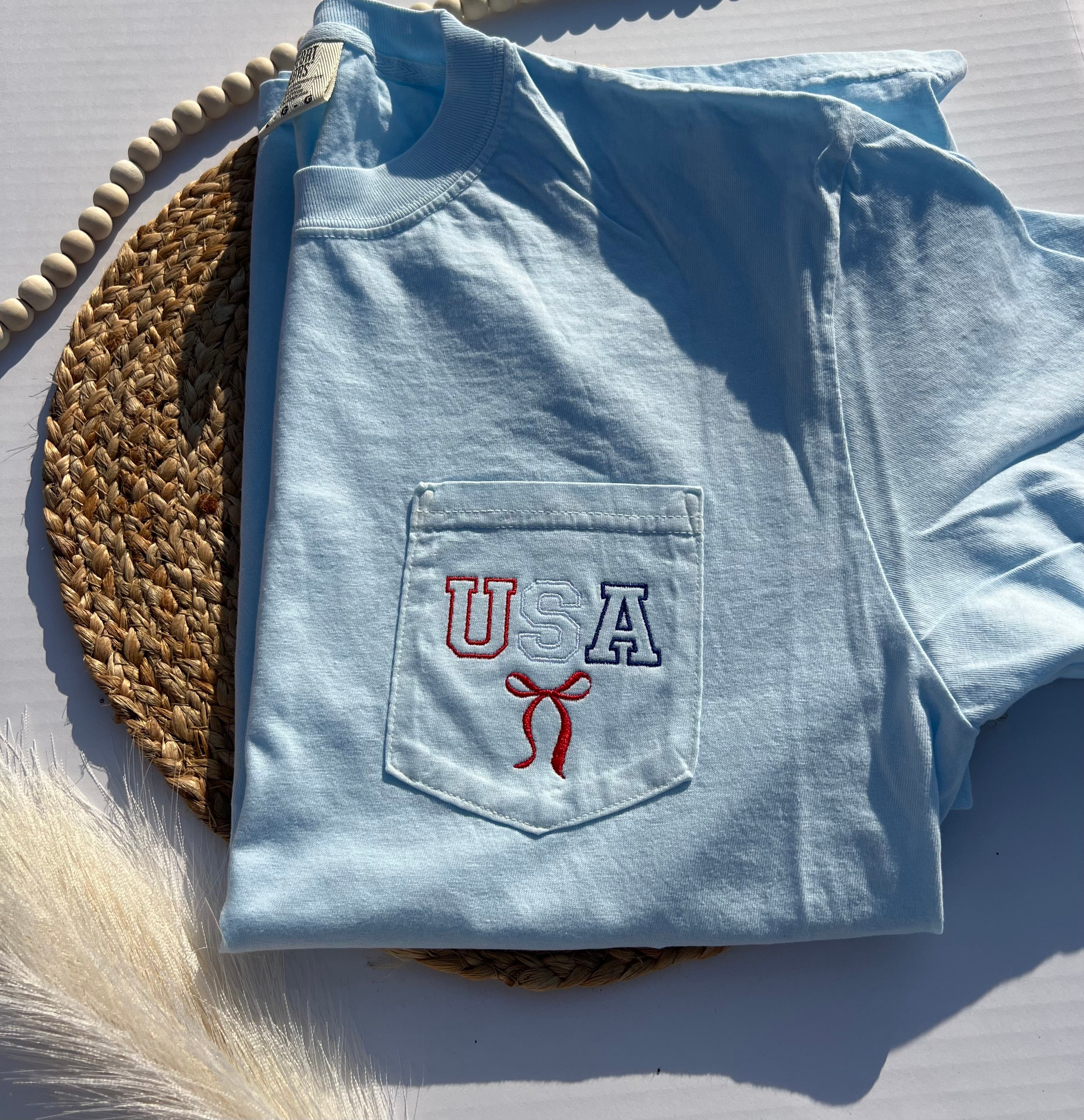 Folded light blue t-shirt with 'USA'  and  a red bow embroidery 