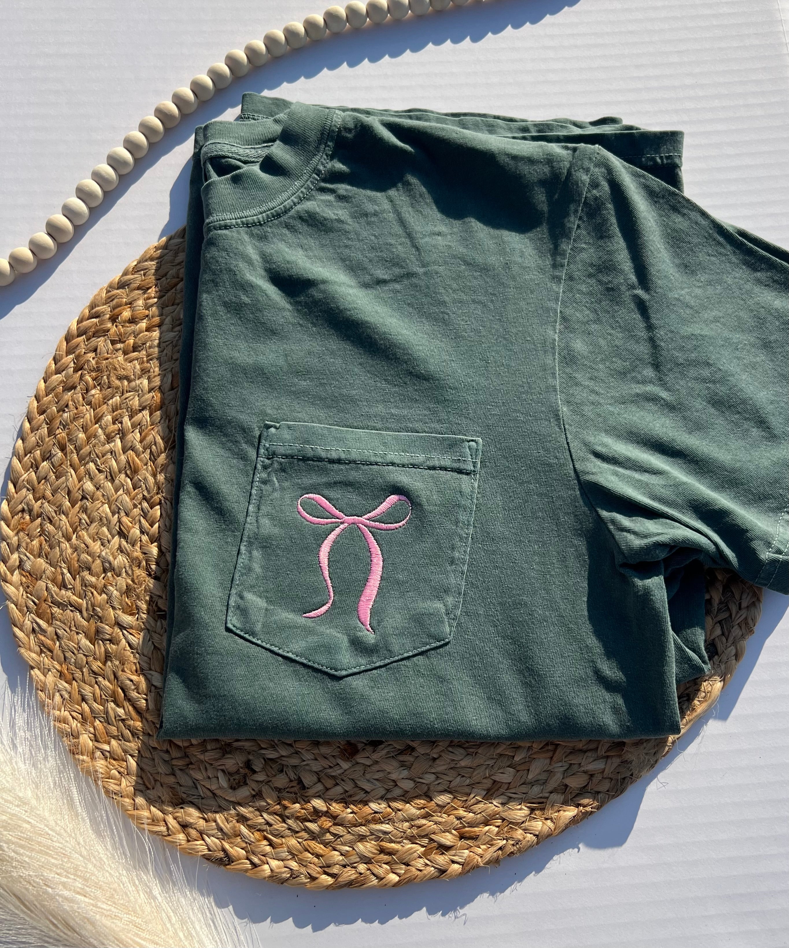 Green t-shirt with a pink bow design on a woven mat