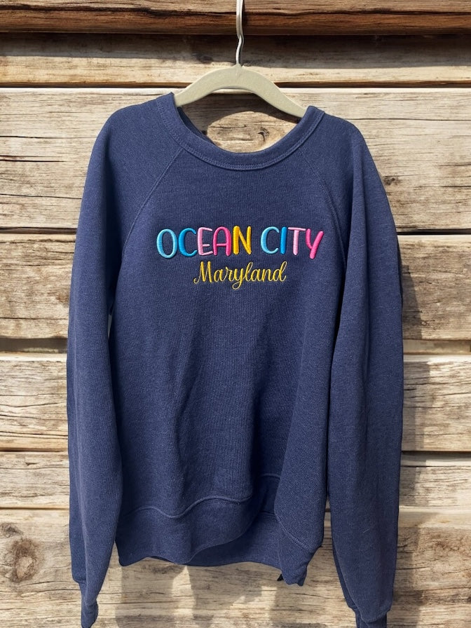 Navy blue sweatshirt with 'Ocean City Maryland' text on a wooden background