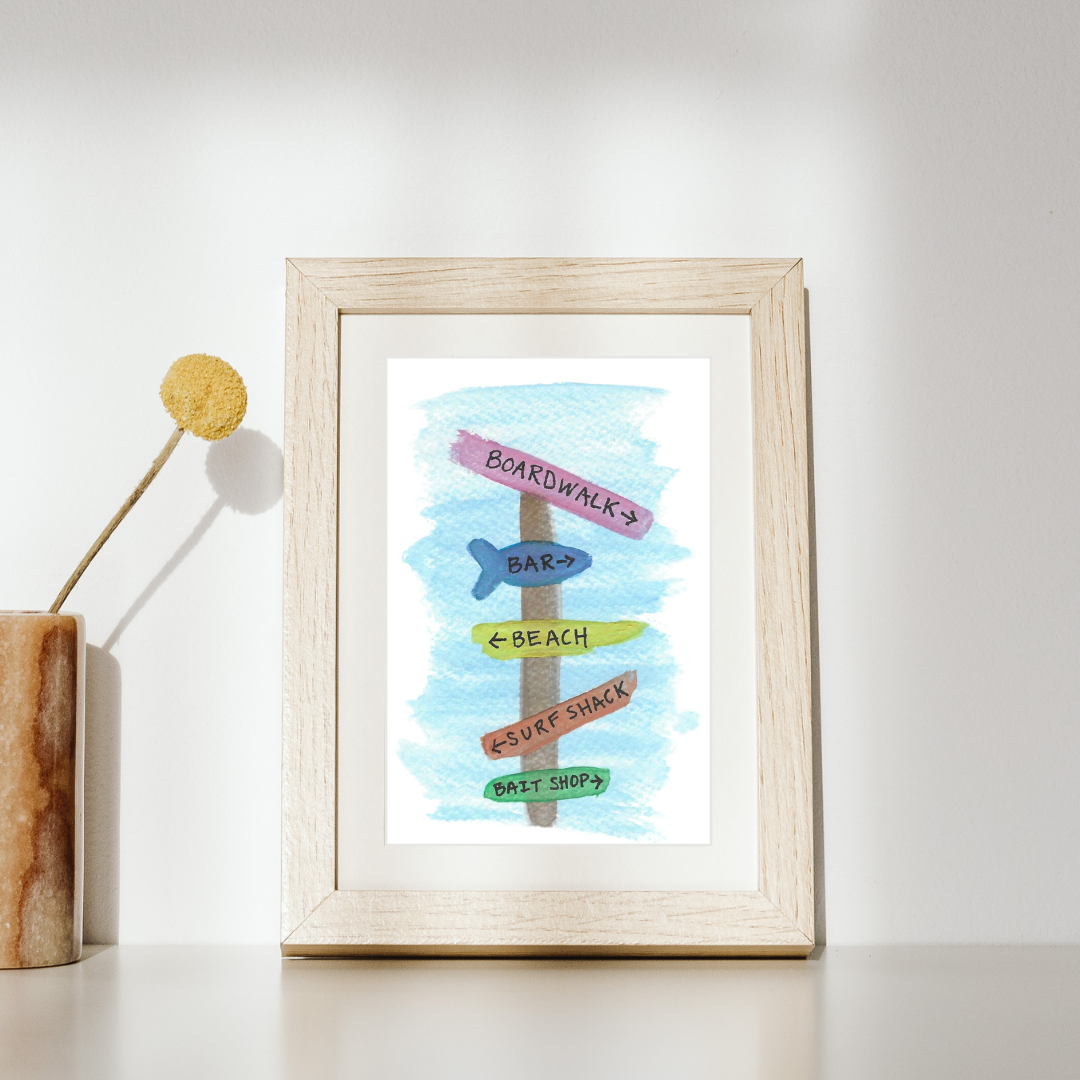 Framed artwork of a beach-themed signpost with colorful text on a white background