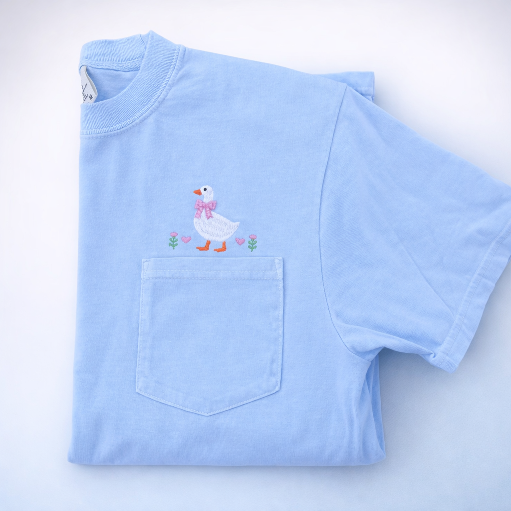 Light blue t-shirt with a goose and flowers embroidered above a pocket