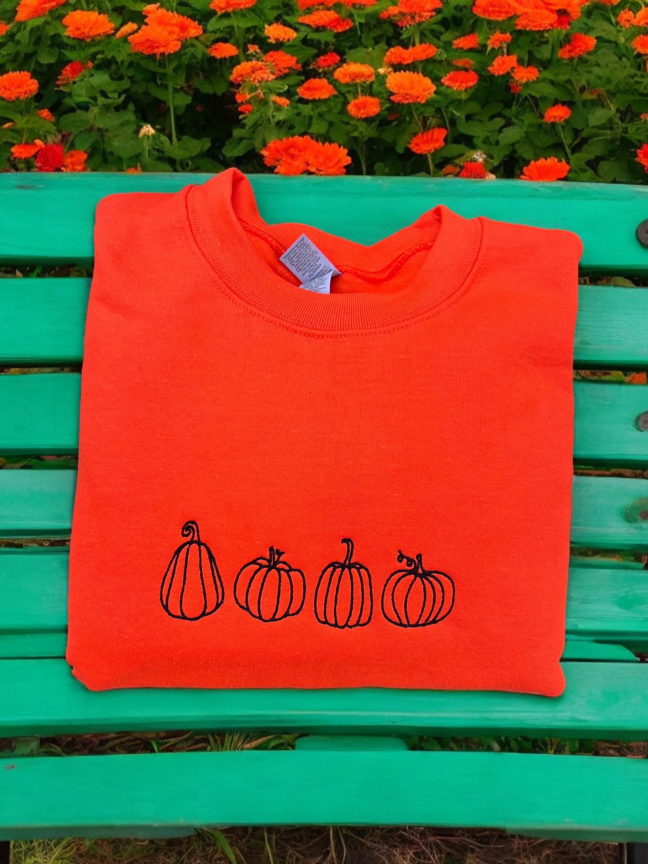 Orange sweatshirt embroidered with black pumpkins. 